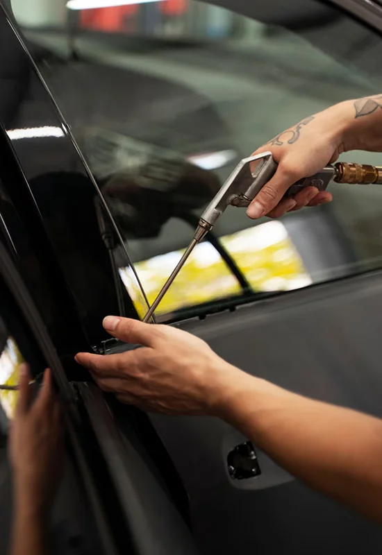 Person using a compressed air tool to clean the gap between a car window and door frame.