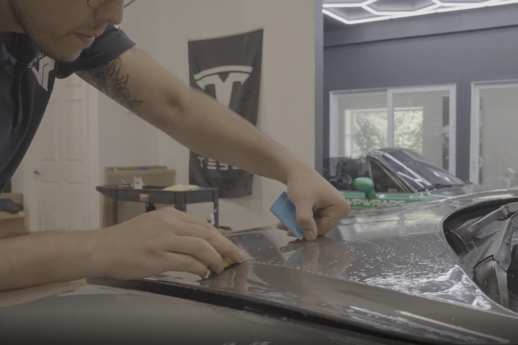 A technician applies paint protection film to a vehicle's hood using a squeegee and cloth, demonstrating professional prep and installation—key elements to compare when evaluating PPF quotes.