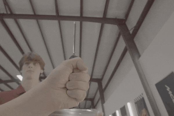 A technician dramatically demonstrates the flexibility of a paint protection film by poking it with a screwdriver without causing damage, highlighting the film’s durability and self-healing properties.