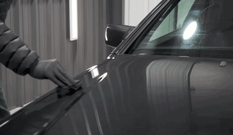 Gloved hand wipes a clean, glossy car hood in preparation for ceramic coating.