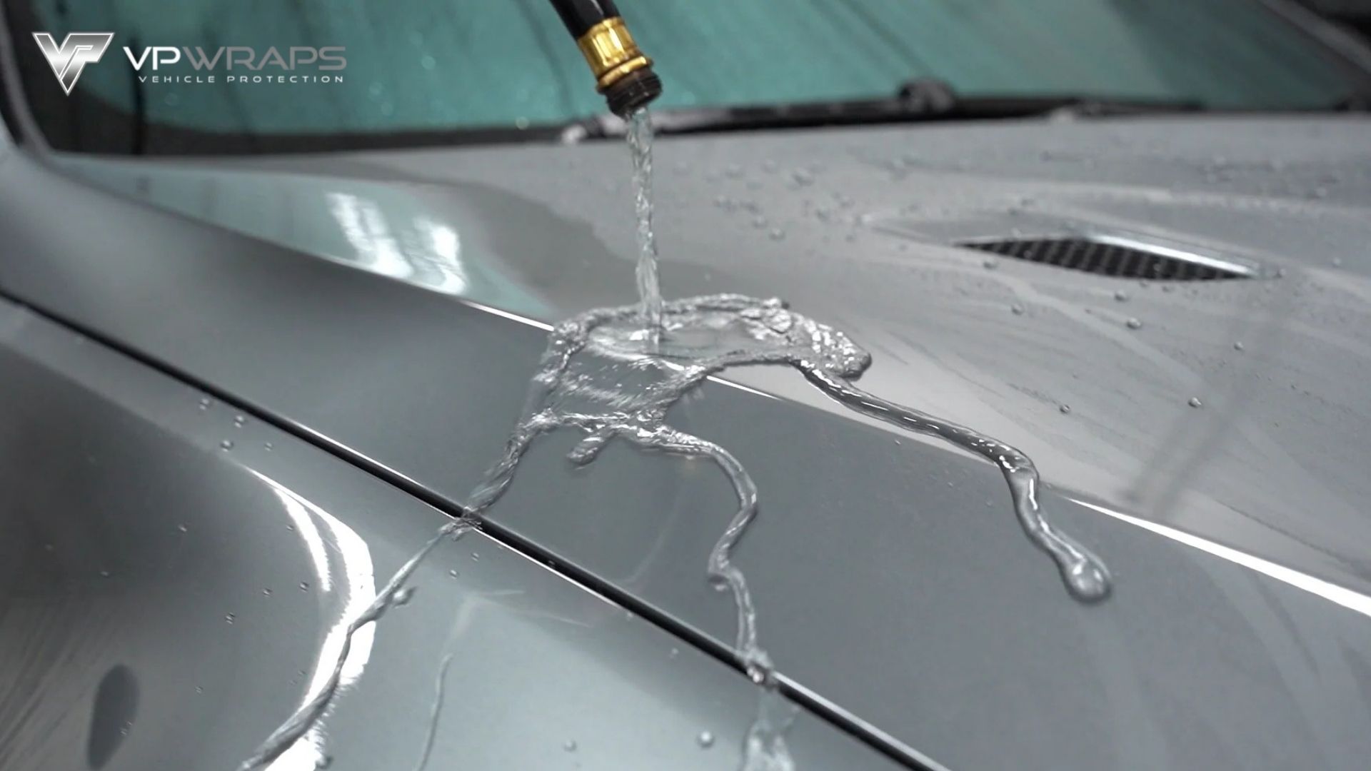 Water beads and sheets off a silver car hood treated with ceramic coating, demonstrating hydrophobic protection.